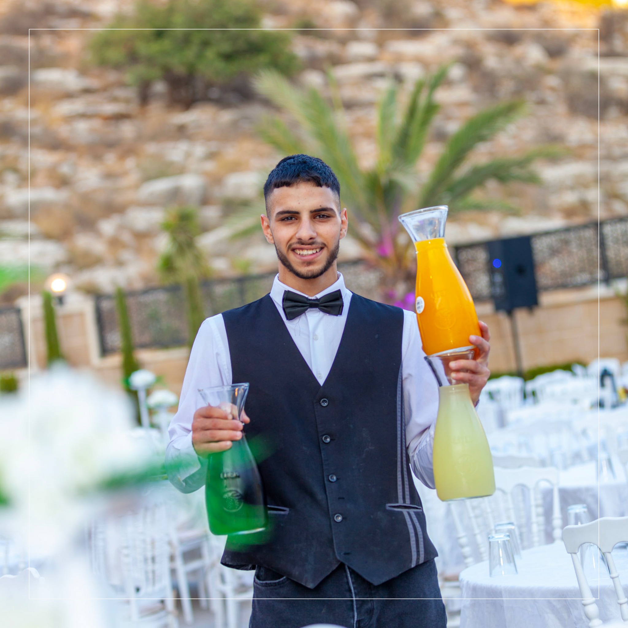 نادل يحمل أباريق من العصير الطازج مع نخيل وتلال رام الله في الخلف